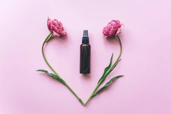 Frascos cosméticos hechos de vidrio ámbar y tulipanes rosados sobre un fondo rosa. — Foto de Stock