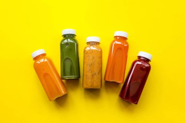 Fresh juices or smoothies of fruits and vegetables in bottles on a yellow background. Flat lay, top view.