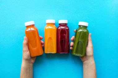 Mavi arka planda meyve suyu veya smoothie ile plastik şişeleri tutan kadın.. 