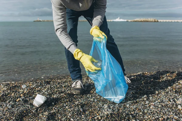 A man volunteer collects garbage on a dirty beach. The concept of waste recycling, environmental cleaning