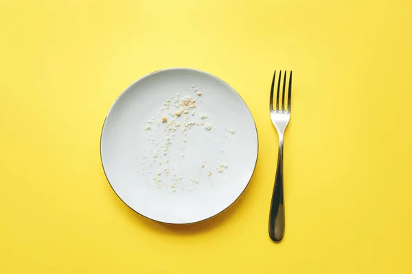 Empty plate with crumbs and fork on it on yellow background. — Stock Photo, Image
