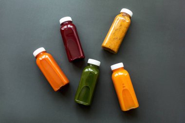 Taze meyve suları ya da meyve ve sebze kokteylleri gri arka planda şişelerde.. 