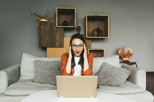 Una joven muy sorprendida con gafas trabaja desde casa. Un estudiante está estudiando en casa o un freelancer. — Foto de Stock