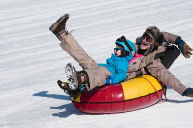 Mother and son snow tubing down hill clipart
