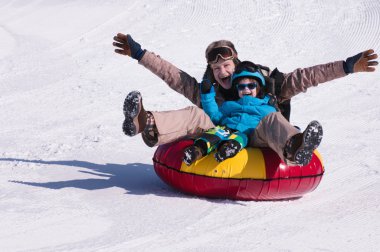 Mother and son snow tubing down hill clipart