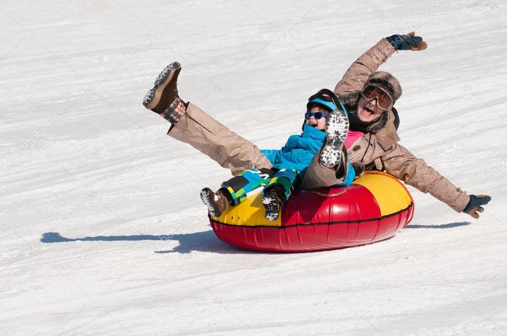 Mother and son snow tubing down hill