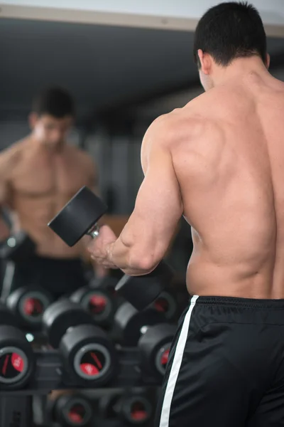 Muskulöser junger Mann trainiert mit Kurzhanteln im Fitnessstudio — Stockfoto