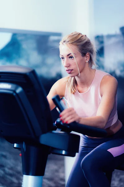 Blond woman using gym bicycle — Stock Photo, Image