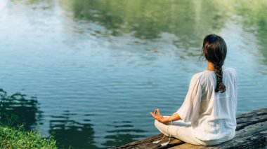 Yoga İnzivası. Nilüfer pozisyonunda oturan ve gölün kenarında meditasyon yapan huzurlu genç bir kadın.
