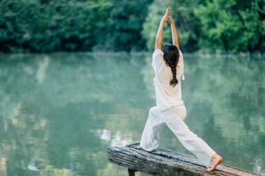 Göl kenarındaki Yoga Savaşçı 1 Poz Veren Genç Kadın veya Virabhadrasana I 