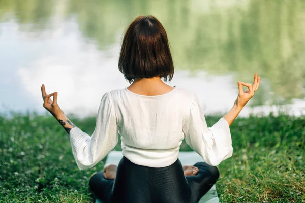 若い女性蓮の位置に座って 自然の中で水の近くに瞑想を練習 — ストック写真
