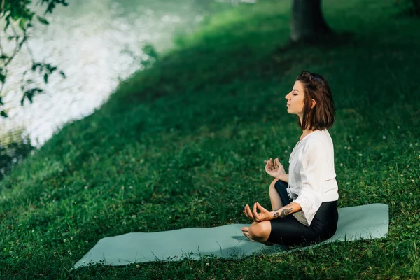 若い女性蓮の位置に座って 自然の中で水の近くに瞑想を練習 — ストック写真
