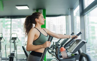 Genç ve çekici bir kadın spor salonunda eliptik egzersiz makinesiyle ısınıyor. Fitness, sağlıklı yaşam tarzı konsepti.