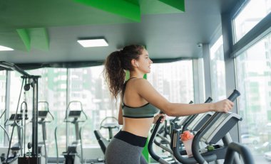 Genç ve çekici bir kadın spor salonunda eliptik egzersiz makinesiyle ısınıyor. Fitness, sağlıklı yaşam tarzı konsepti.