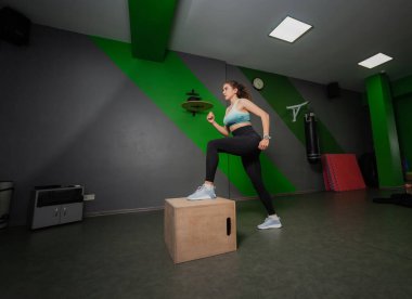 Genç, formda bir kadın spor dersinde tahta bir kutuya basıyor. Fonksiyonel eğitim, egzersiz.