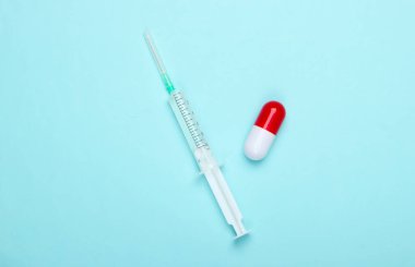 Düz ilaç kompozisyonu. İlaç kapsülü, mavi pastel arka planda aşılı şırınga. Üst görünüm