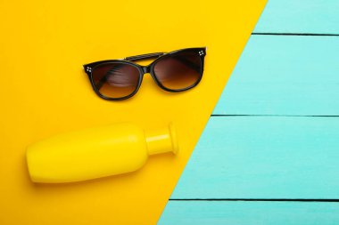 Plaj tatili için düz kompozisyon. Güneş gözlüğü, güneş kremi şişesi ve ahşap mavi arka plan. Üst görünüm
