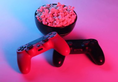 İki oyun pedi ve bir kase patlamış mısır. Neon pembe ışık. Oyun, eğlence ve eğlence konsepti.