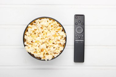 Bir kase patlamış mısır, beyaz arka planda uzaktan kumanda. Boş zaman ve eğlence konsepti. Üst görünüm