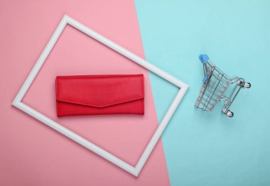 Pembe arka planda beyaz çerçeveli alışveriş arabası ve kırmızı deri cüzdan. Alışveriş konsepti. Üst görünüm