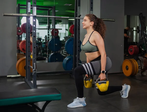 Genç, formda bir kadın spor salonunda kettlebell egzersizi yapıyor. Serbest ağırlık, fonksiyonel eğitim