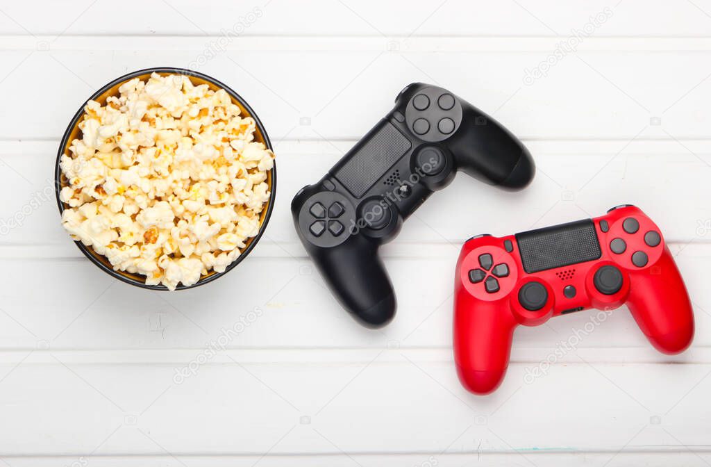 Two gamepads and a bowl of popcorn on white wooden table. Gaming, leisure and entertainment concept. Top view