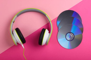Havalı telli kulaklıklar ve pembe pastel arka planda CD 'ler. Müzik aşığı. Retro 90 'lar. Üst görünüm.