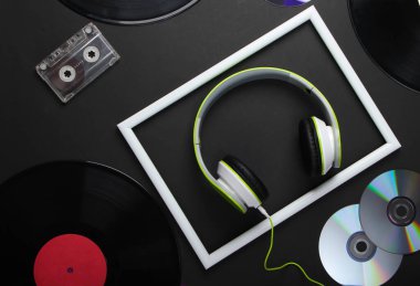 80 'lerin retro medyasından düz kompozisyon. Beyaz çerçeveli stereo kulaklıklar, vinil kayıtlar, ses kasetleri ve siyah arka planda CD 'ler. Müzik aşığı. Üst görünüm.