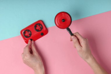 Küçük oyuncak tavayı tutan kadın el ve pembe mavi pastel arka planda fırın. Üst görünüm