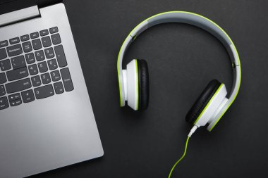 Siyah arka planda kulaklıkları olan bir laptop. DJ, oyun, eğlence ya da eğlence konsepti. Üst Manzara. Düz yatıyordu