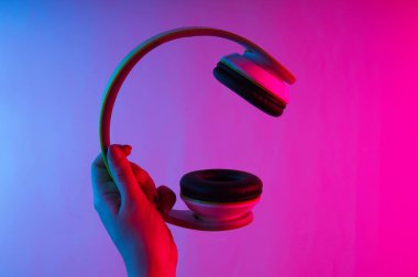 Kadın eli, neon mavi-pembe gradyan ışıklı kablosuz stereo kulaklıkları tutuyor..