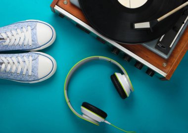 Müzik kulaklığı ve mavi arka planda spor ayakkabısı olan eski bir plak çalar. Retro ortam. Üst Manzara. Düz yatıyordu