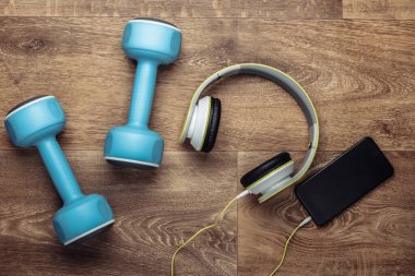 Düz konum spor ve spor kompozisyonu. Dambıllar, ahşap zeminde akıllı telefonlu kulaklıklar. Üst görünüm