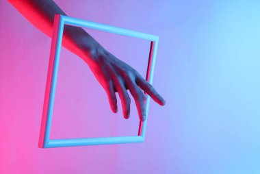 Yaratıcı sanat. Süzülen bir çerçeveden süzülen bir kadın eli, neon holografik ışıkla. Kıvılcım