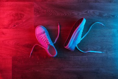 Ahşap bir zeminde, kırmızı-mavi renkte parlayan eski moda spor ayakkabılar. Üst görünüm