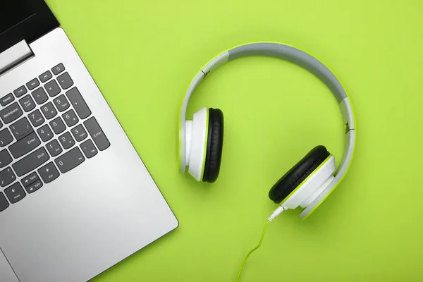 Laptop with headphones on green background. DJ, gaming, entertainment or leisure concept. Top view. Flat lay