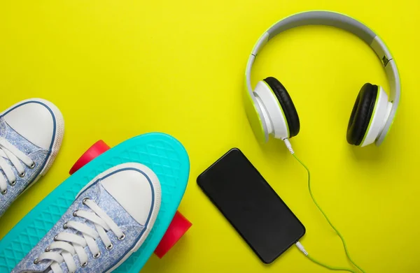 Flat lay hipster stuff. Sneakers on cruiser board and stereo headphones with smartphone on green background. Summer fun. Top view