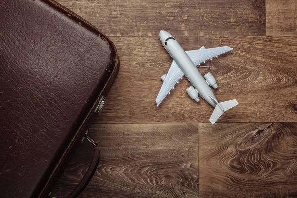 Travel concept. Old luggage and airplane figurine on wooden floor. Flight voyage, trip, journey. Flat lay composition. Top view