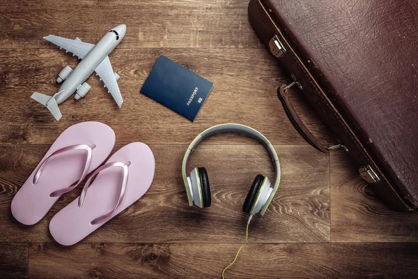 Travel concept. Old luggage, headphones, flip flops, airplane figurine, passport on wooden floor. Flight voyage, trip, journey. Beach vacation. Flat lay composition. Top view