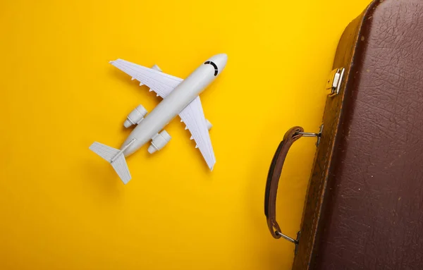 Travel concept. Old luggage and airplane figurine on yellow background. Flight voyage, trip, journey. Flat lay composition. Top view