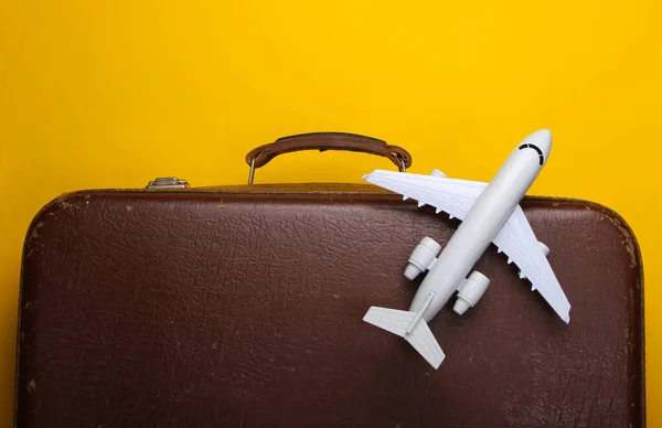 Travel concept. Old luggage and airplane figurine on yellow background. Flight voyage, trip, journey. Flat lay composition. Top view