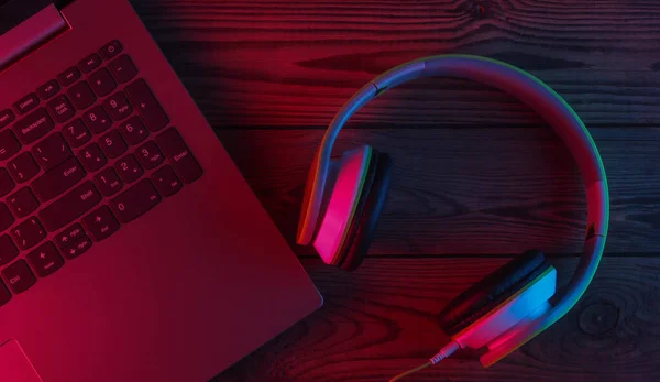 DJ or gaming concept. Laptop and headphones with neon blue-red light. Top view