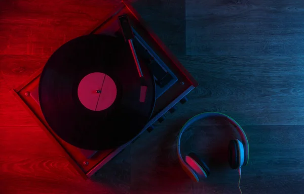立体声耳机和复古乙烯唱机在木制地板上与蓝红色霓虹灯 明亮的光芒 顶部视图 — 图库照片