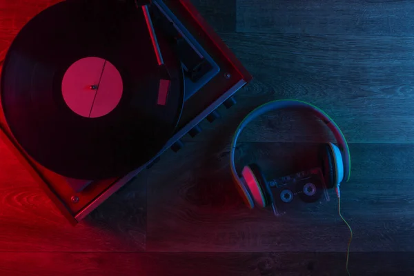 立体声耳机和复古乙烯唱机在木制地板上与蓝红色霓虹灯 明亮的光芒 顶部视图 — 图库照片