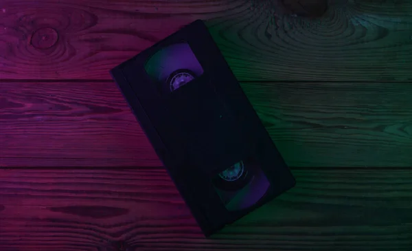 Video Cassette on wooden background. Neon purple green light. Gradient glow. Retro media and entertainment. Top view