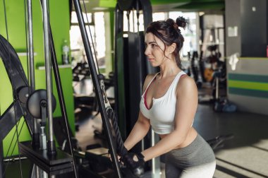 Spor salonundaki egzersiz makinesinde kollarını uzatarak idman yapan sıska bir kadın.