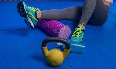 Formda bir kadın, bacağında köpük rulo kullanarak gerginliği azaltır ve spor salonundaki eğitimden sonra kas ağrısına yardımcı olur.