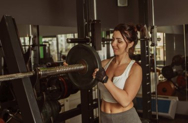 Mükemmel vücutlu genç bir kadın spor salonunda bir halter diski tutuyor.