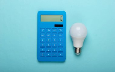 Enerji tasarrufu. Mavi pastel arka planda kurşun ampullü bir hesap makinesi. Üst görünüm