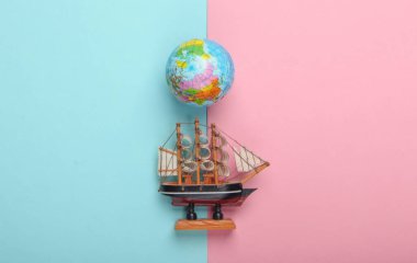 Dünyayı dolaşmak, deniz yolculuğu. Globe, mavi pembe pastel arka planda gemi figürü. Üst Manzara. Minimalizm. Düz yatıyordu